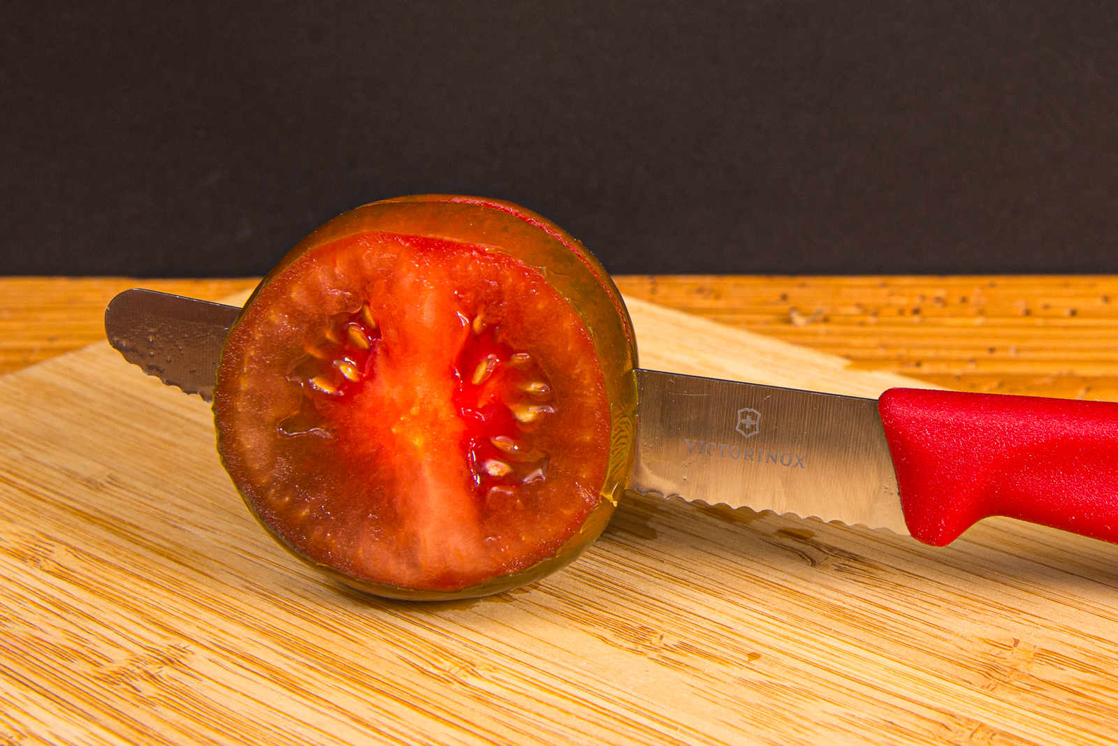 Victorinox Tomatenmesser mit rotem Griff schneidet eine frische Tomate &ndash; scharfes K&uuml;chenmesser mit individueller Logogravur als Werbeartikel.