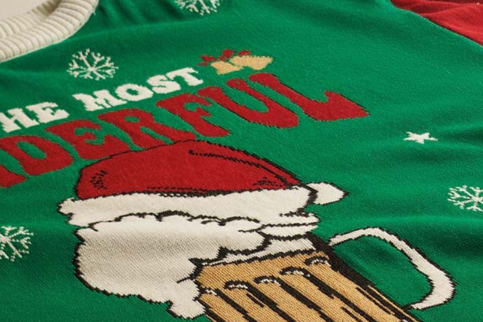 Detailaufnahme eines gr&uuml;nen Ugly Christmas Sweaters mit Bierkrug-Motiv, Santa-M&uuml;tze und Schneeflocken im Jacquard-Strick.