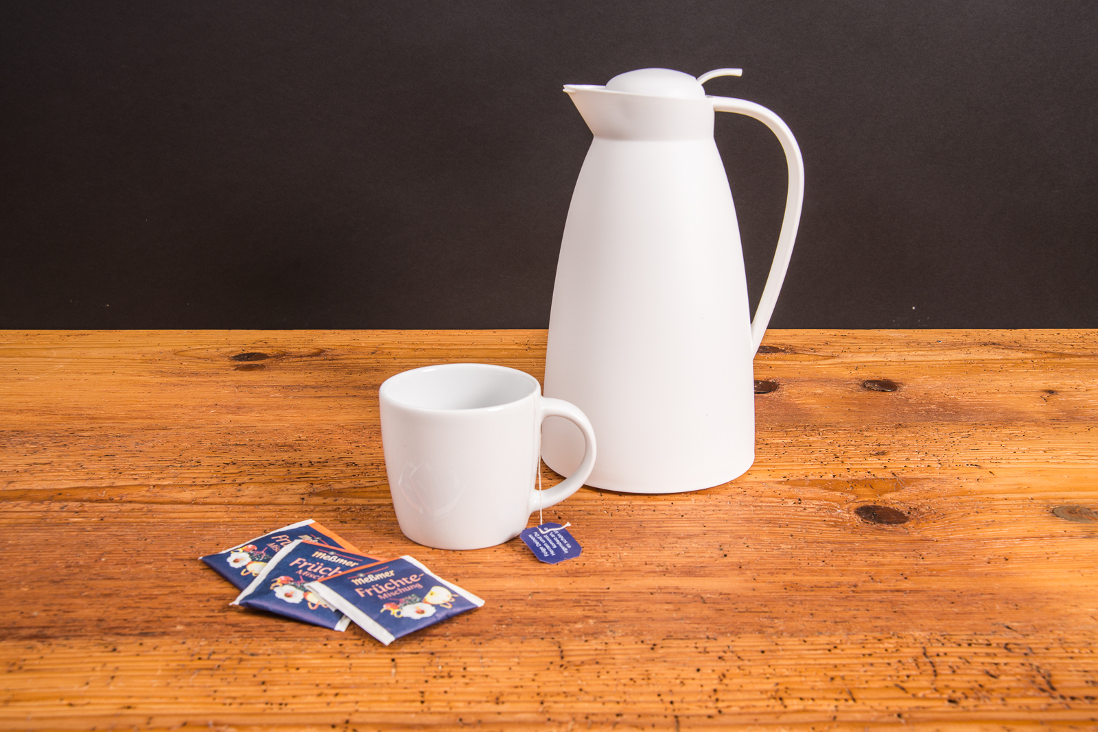 Wei&szlig;e alfi Isolierkanne ECO mit Tasse und Teebeuteln auf Holztisch &ndash; nachhaltige Thermoskanne als Werbeartikel mit Logo.