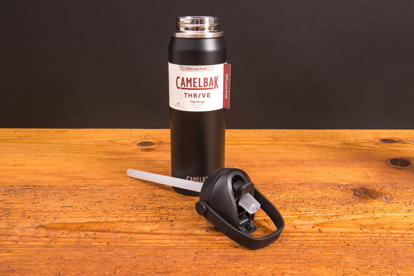 CamelBak Thrive Edelstahl-Trinkflasche in Schwarz mit abgenommenem FlipStraw-Verschluss &ndash; Detailansicht der 750-ml-Isolierflasche als hochwertiges Werbegeschenk mit Logo von werbemaxauf Holztisch.