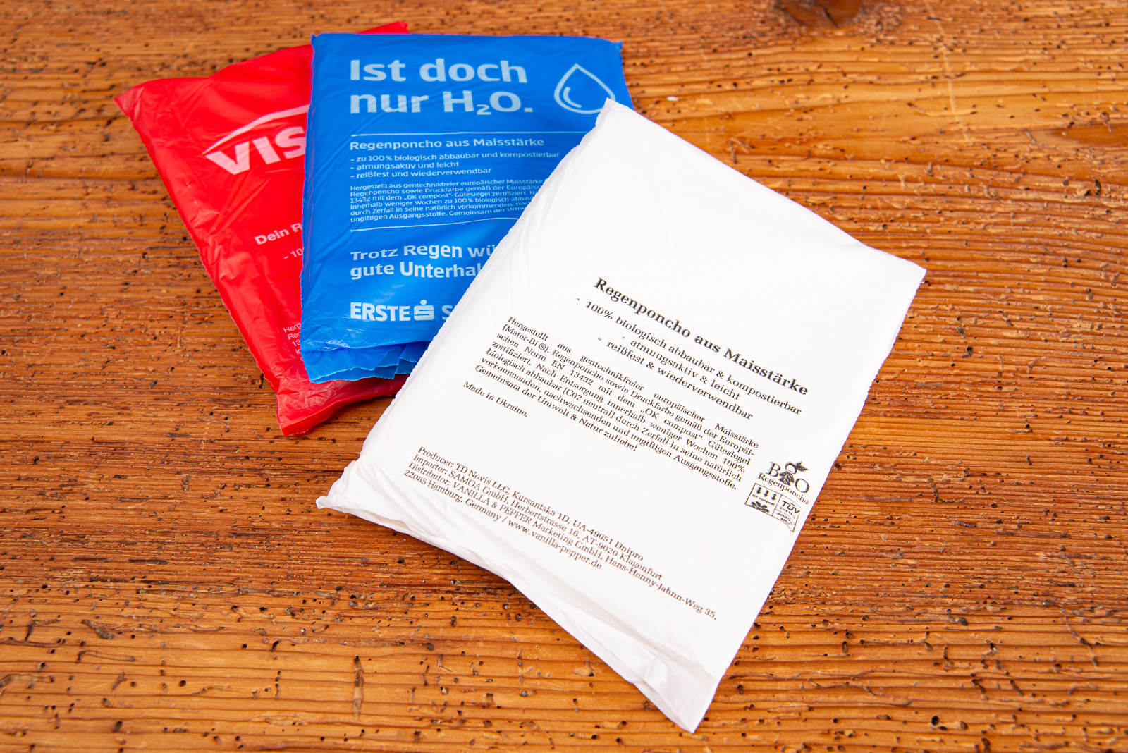 Mehrere farbige Verpackungen biologisch abbaubarer Regenponchos aus Maisst&auml;rke mit individuellen Logos &ndash; nachhaltige Regencapes als Werbeartikel und Festival-Giveaways von werbemax.