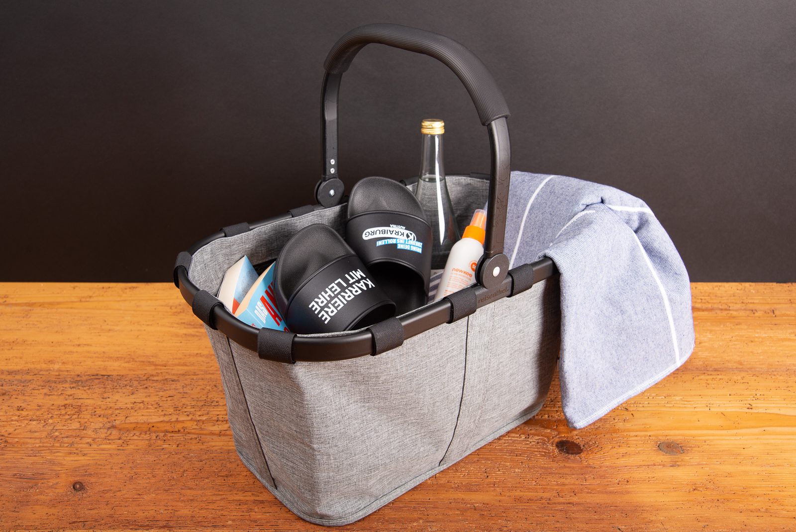 Reisenthel Carrybag Twist Silver in Grau, bef&uuml;llt mit Sommerutensilien wie Handtuch, Sandalen und Getr&auml;nk &ndash; stilvoller Einkaufskorb als hochwertiges Werbegeschenk oder Mitarbeiterpr&auml;sent.