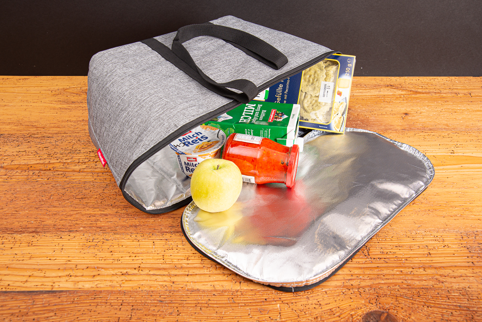 Reisenthel K&uuml;hltasche coolerbag in twist silver, bef&uuml;llt mit Lebensmitteln ist eine praktische Isoliertasche als hochwertiges Werbegeschenk f&uuml;r Mitarbeiter und Kunden liegend offen auf Holztisch.