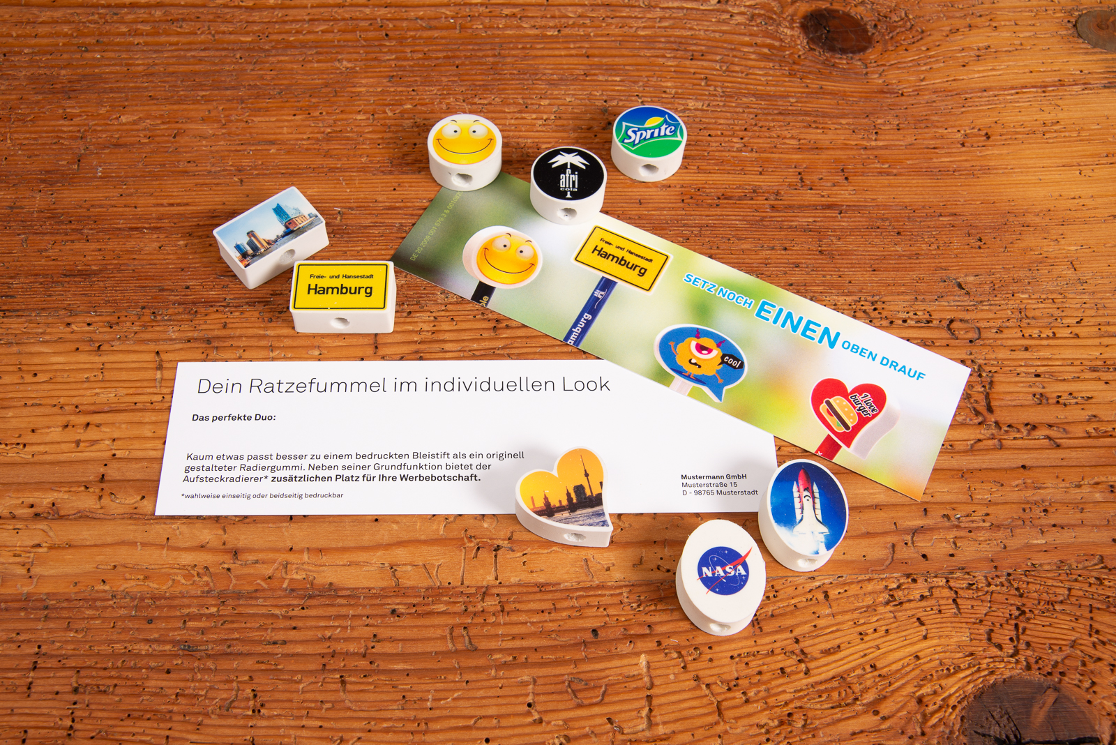 Aufsteckradierer individuell bedruckt als g&uuml;nstiger Werbeartikel &ndash; verschiedene Radiergummi-Formen mit Logos und Motiven auf Holztisch.