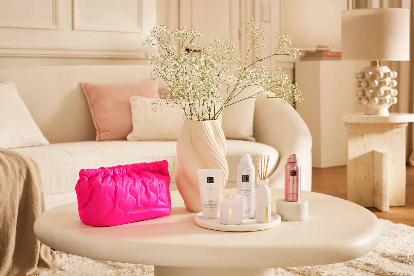Rituals Sakura Geschenkset mit pinker Kosmetiktasche und Pflegeprodukten auf Wohnzimmertisch.