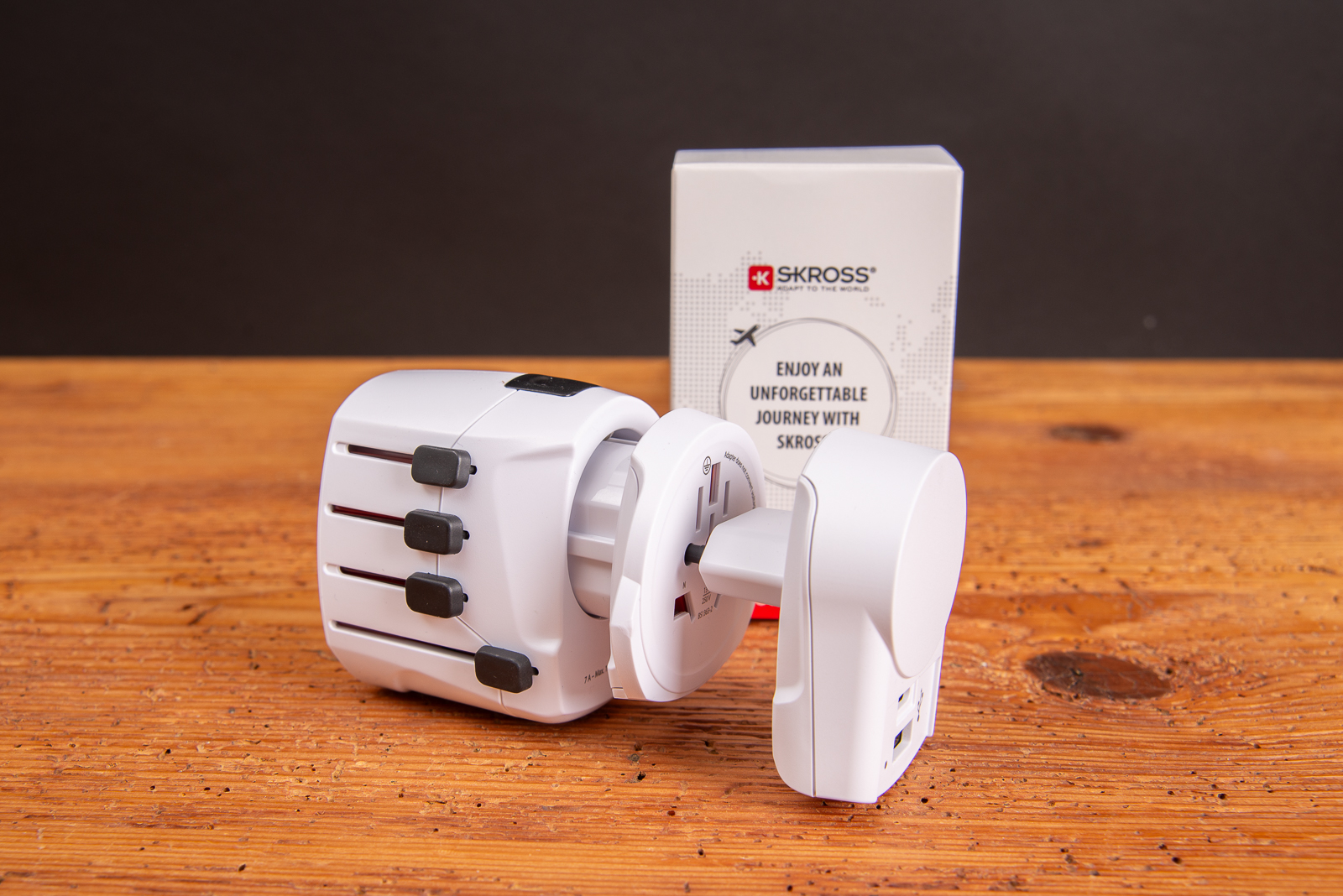 SKROSS PRO+USB Reiseadapter mit Verpackung auf Holztisch &ndash; ideales Werbegeschenk f&uuml;r internationale Gesch&auml;ftsreisen.