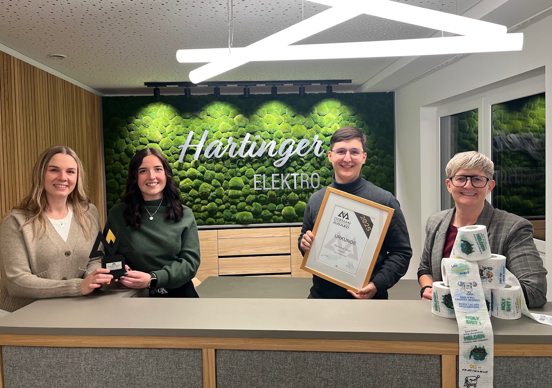 Team von Elektro Hartinger mit dem German Marketing Award 2025, der pr&auml;mierten Urkunde und dem kreativen Werbemittel bedrucktes Toilettenpapier, entwickelt von werbemax.