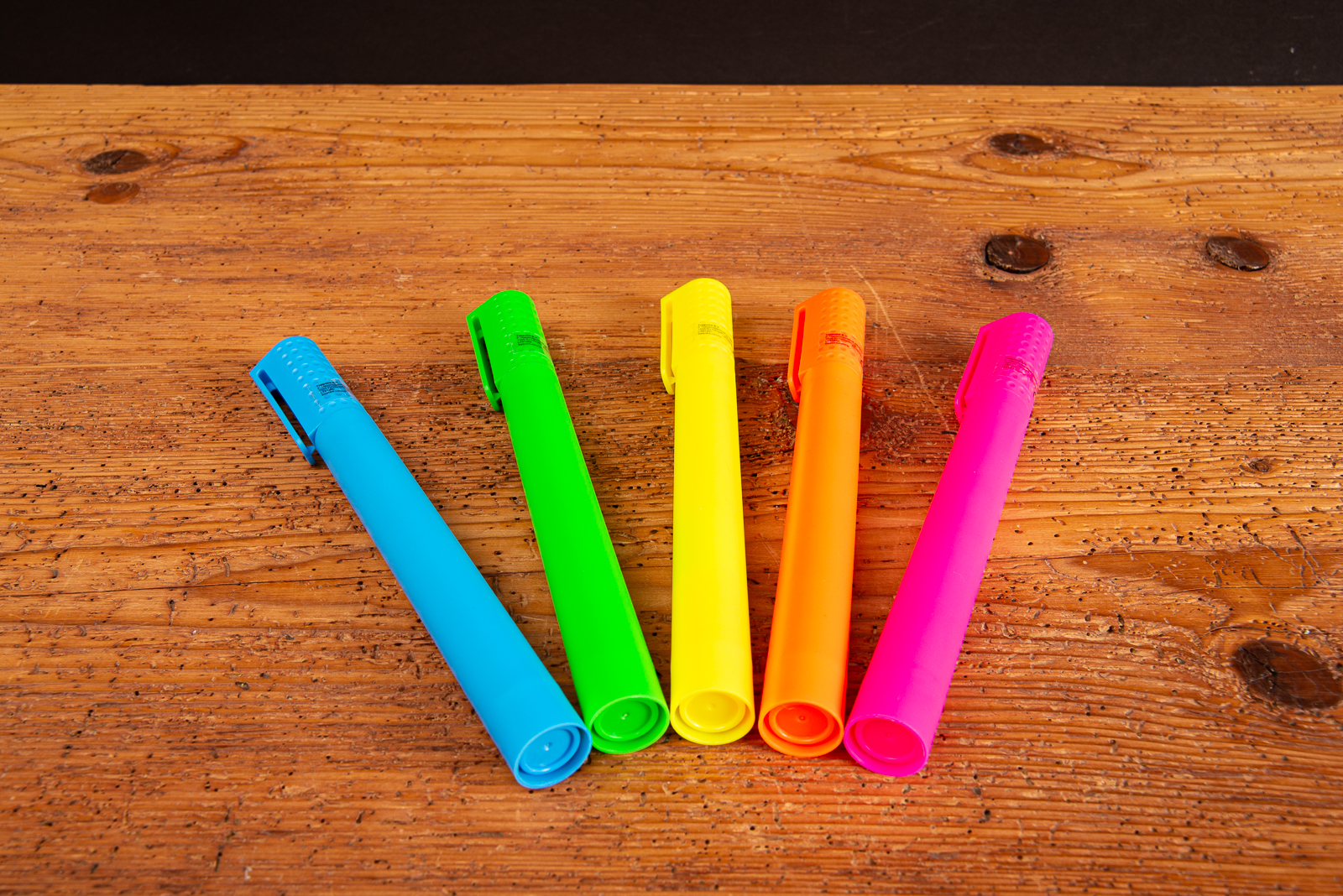 F&uuml;nf farbige Jumbo Textmarker im XL-Format als Duftstifte auf Holztisch &ndash; auff&auml;llige Werbemittel f&uuml;r Messen, kreative Giveaway-Idee mit hohem Wiedererkennungswert und gro&szlig;er Werbefl&auml;che f&uuml;r Logo-Druck.