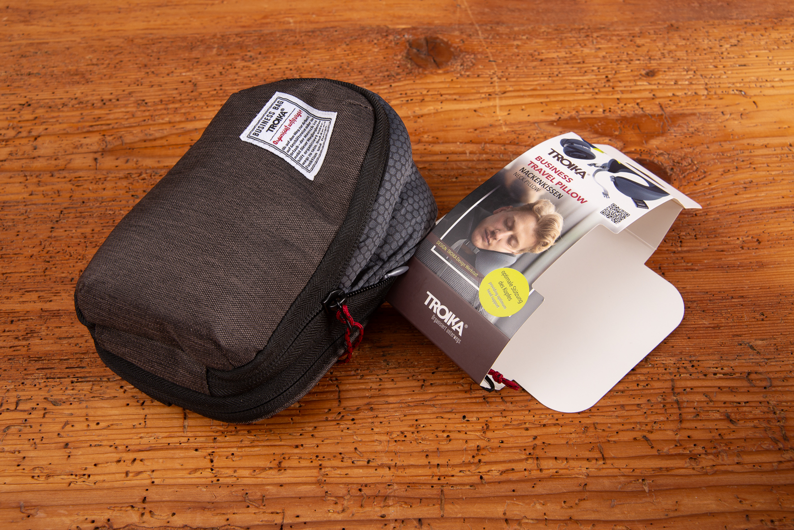 Troika Nackenkissen mit Logo zusammengefaltet in Transporttasche aus Stoff auf Holzoberfl&auml;che.