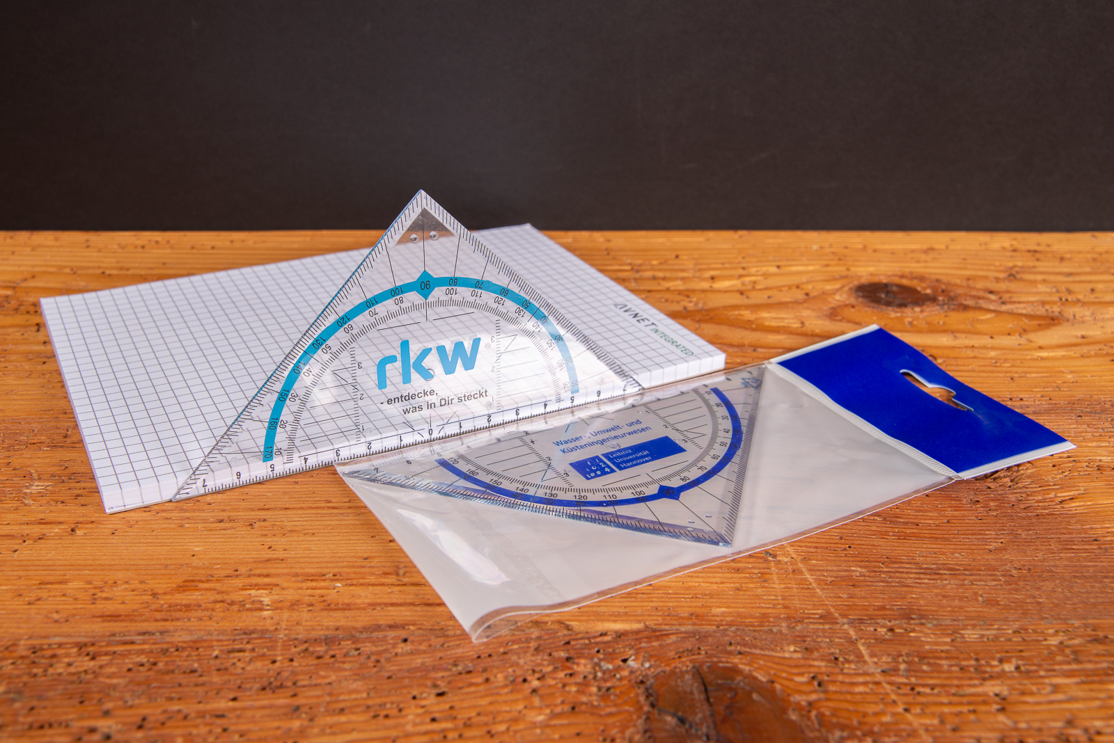 Geodreieck mit Logo auf kariertem Papier &ndash; klassisches Werbegeschenk f&uuml;r Sch&uuml;ler und Azubis