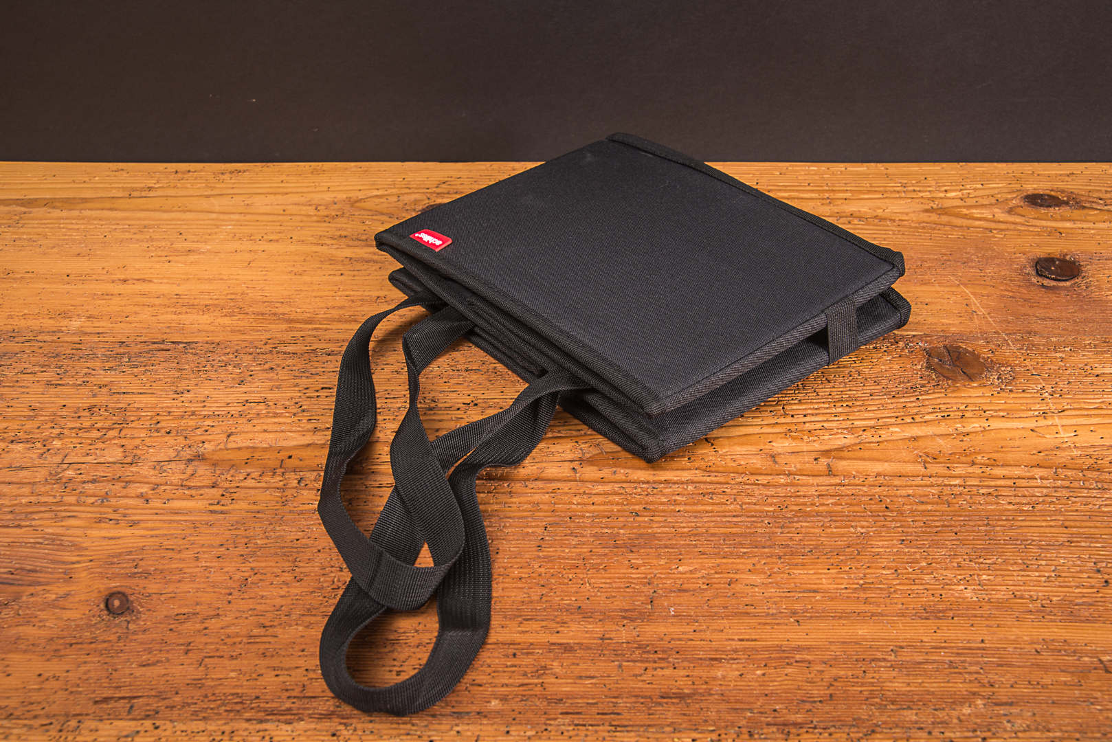 Schwarzer Kofferraum Organizer im flach gefalteten Zustand mit Tragegriffen &ndash; ideal als platzsparender Werbeartikel von werbemax