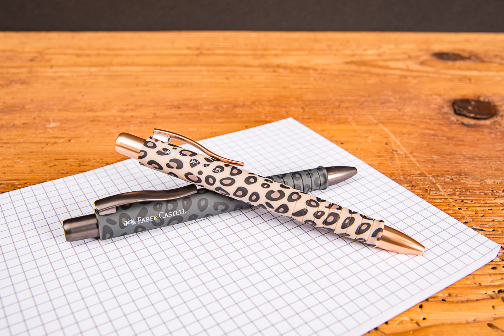 Faber-Castell Kugelschreiber im Leo-Design als hochwertiger Werbekugelschreiber mit Logo auf kariertem Notizblock.