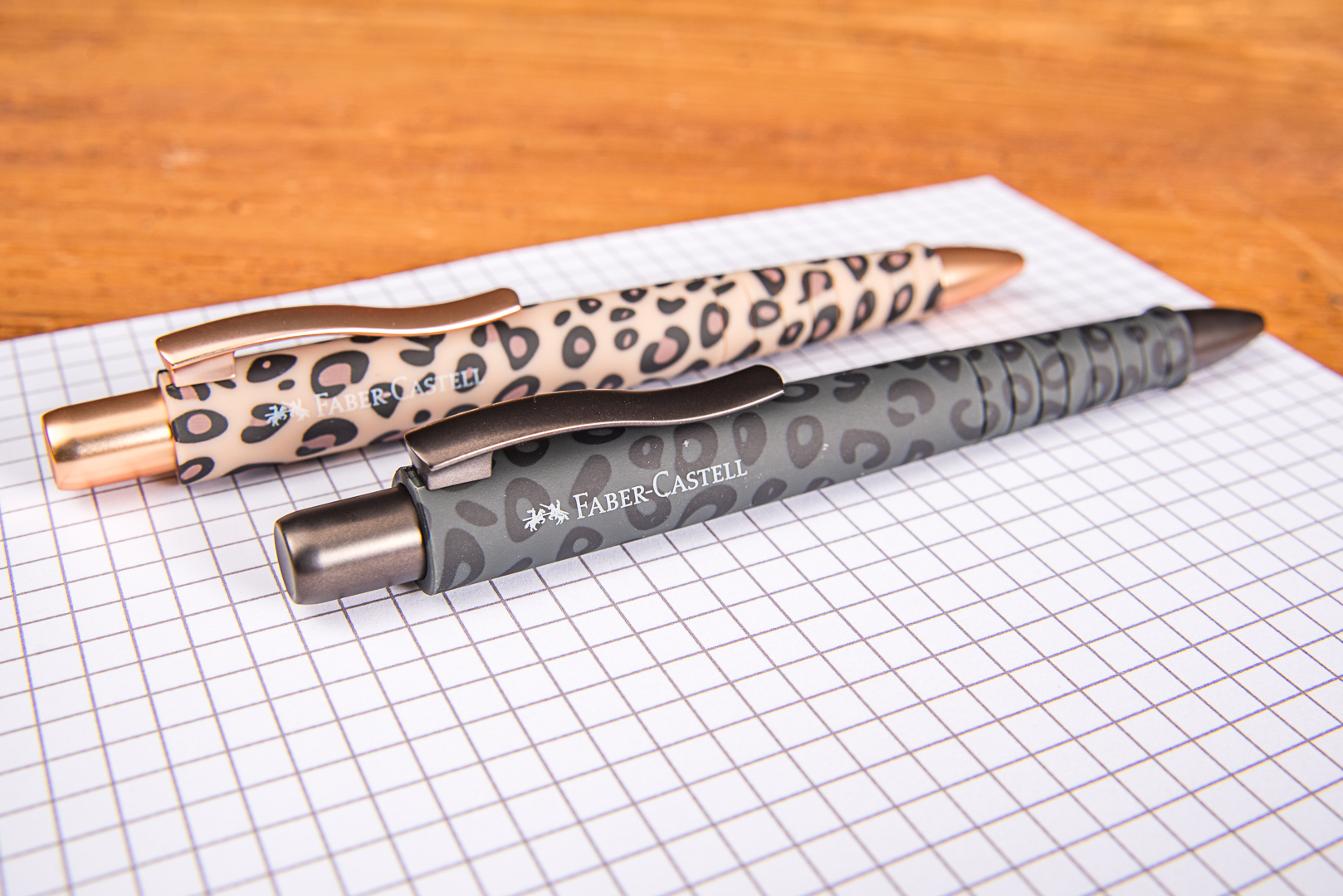 Faber-Castell Kugelschreiber im Leo-Design als hochwertiger Werbeartikel mit Logo auf kariertem Papier platziert.