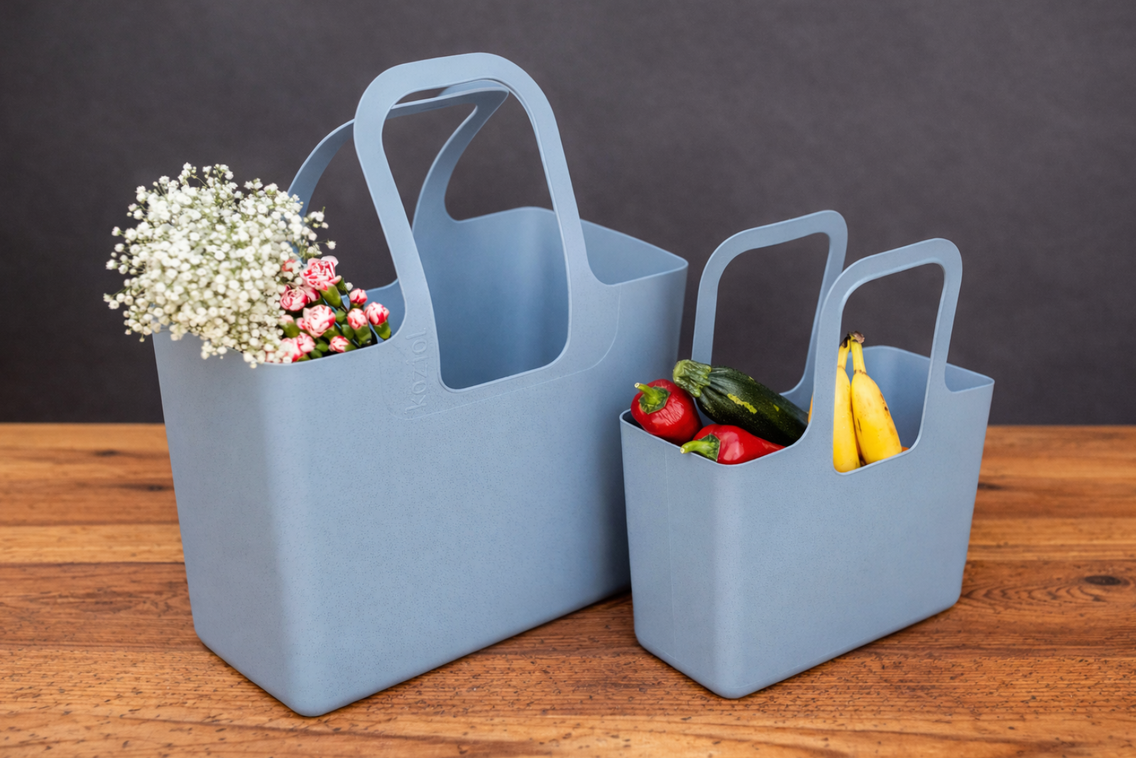 Koziol Tasche XL und kleine Tasche in Blau als Werbemittel mit Inhalt wie Obst und Blumen auf Holztisch.