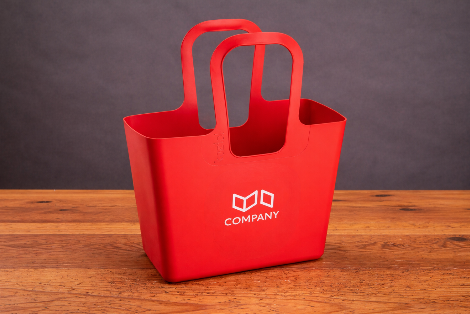 Koziol Tasche XL in Rot mit Logo als hochwertiger Werbeartikel auf Holztisch vor dunklem Hintergrund.