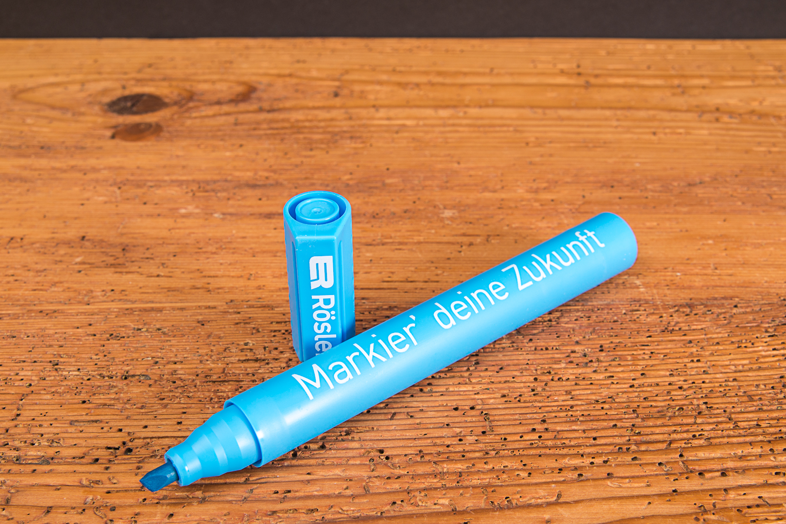 Blauer Textmarker mit Logo als Werbeartikel und Giveaway f&uuml;r Jugendliche &ndash; gro&szlig;er Markierstift mit Werbedruck auf Holzuntergrund.