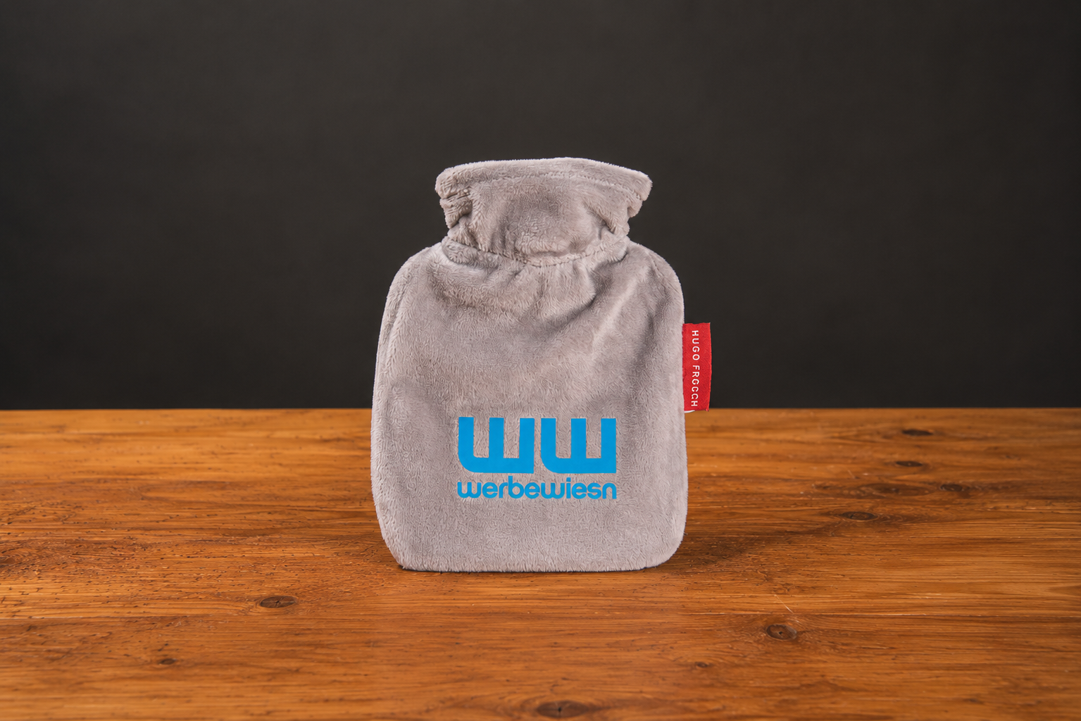 Mini W&auml;rmflasche Made in Germany mit Logo als Druck auf dem abnehmbaren Veloursbezug in Grau. 