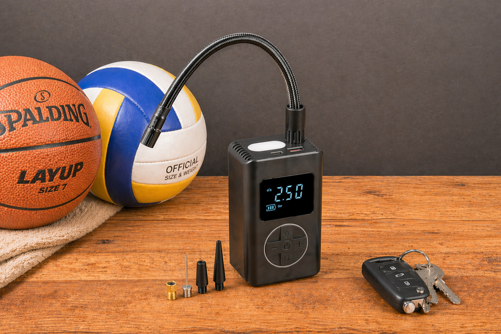 PUMP Universal Akkupumpe f&uuml;r Reifen und B&auml;lle mit digitalem Display auf einem Holztisch neben einem Basketball und Volleyball.