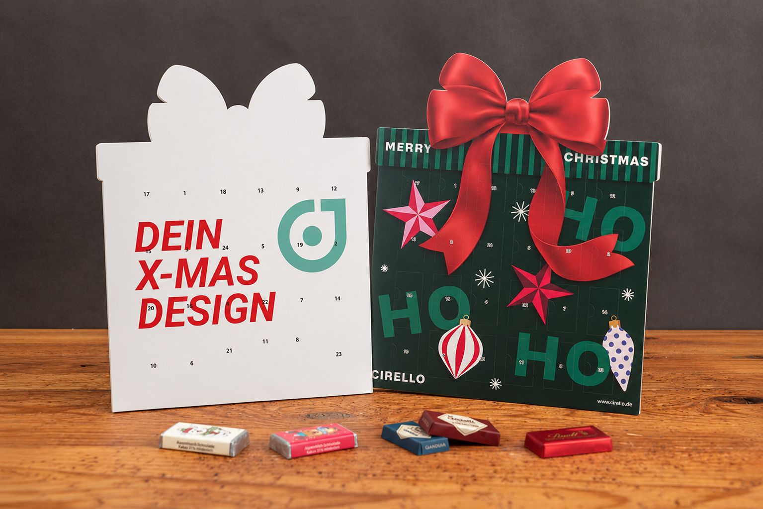 Zwei Geschenk-Adventskalender mit Schokolade von werbemax auf rustikalem Holztisch vor dunkler Wand &ndash; individuelle Weihnachtsmotive mit Schleife und modernem X-MAS-Design.