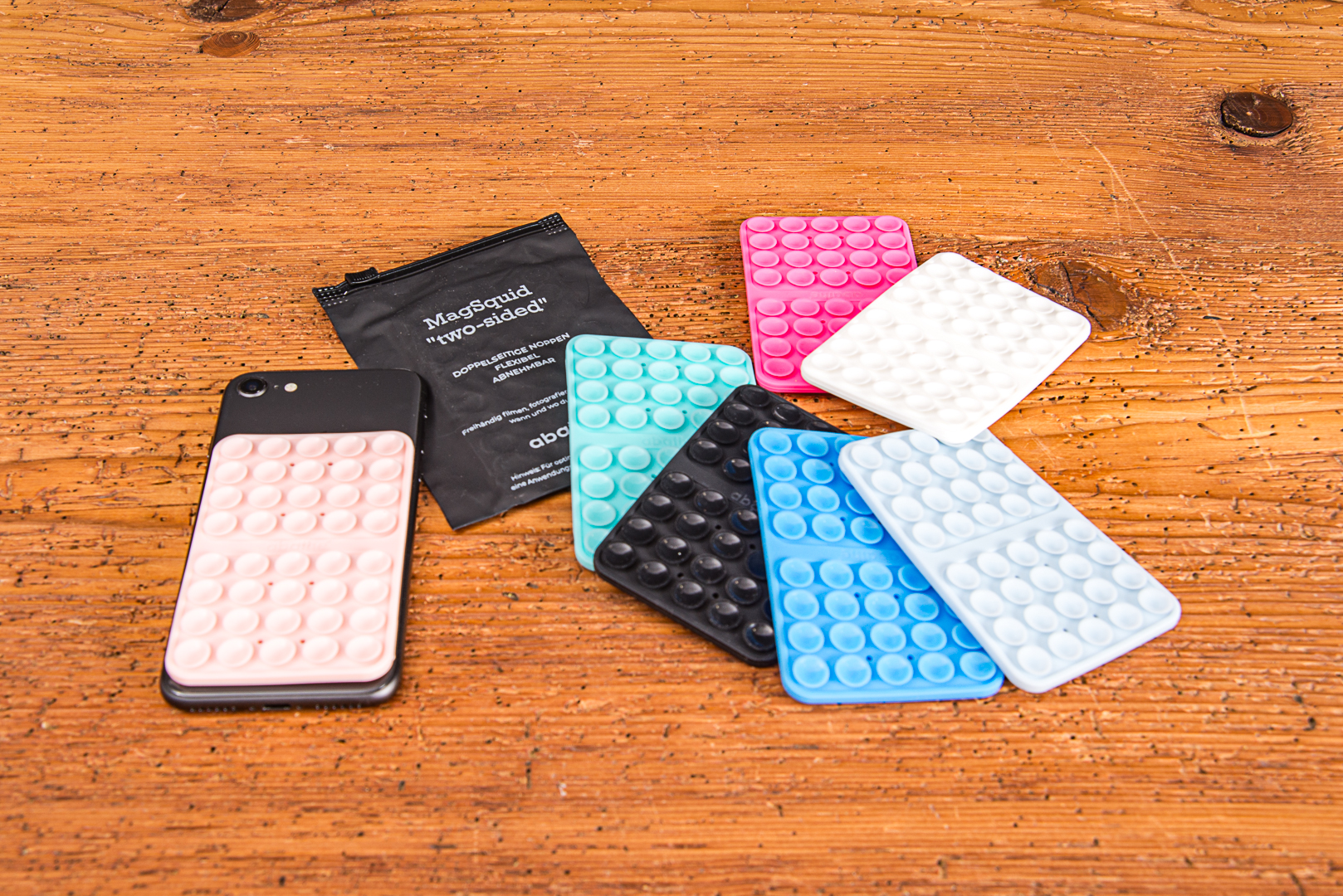MagSquid Two Sides Saugnapf-Handyhalterungen in verschiedenen Farben mit schwarzer Produktverpackung auf einem Holztisch.