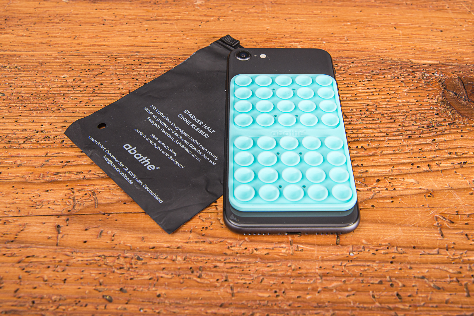T&uuml;rkises Silikon-Saugnapf-Pad auf einem Smartphone mit flacher, schwarzer Polybeutel-Produktverpackung als Zubeh&ouml;r f&uuml;r Content Creator.