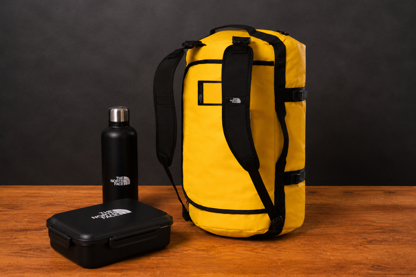 The North Face Duffel Bag auf Holztisch mit Trinkflasche und Lunchbox als hochwertiger Werbeartikel und Mitarbeitergeschenk.