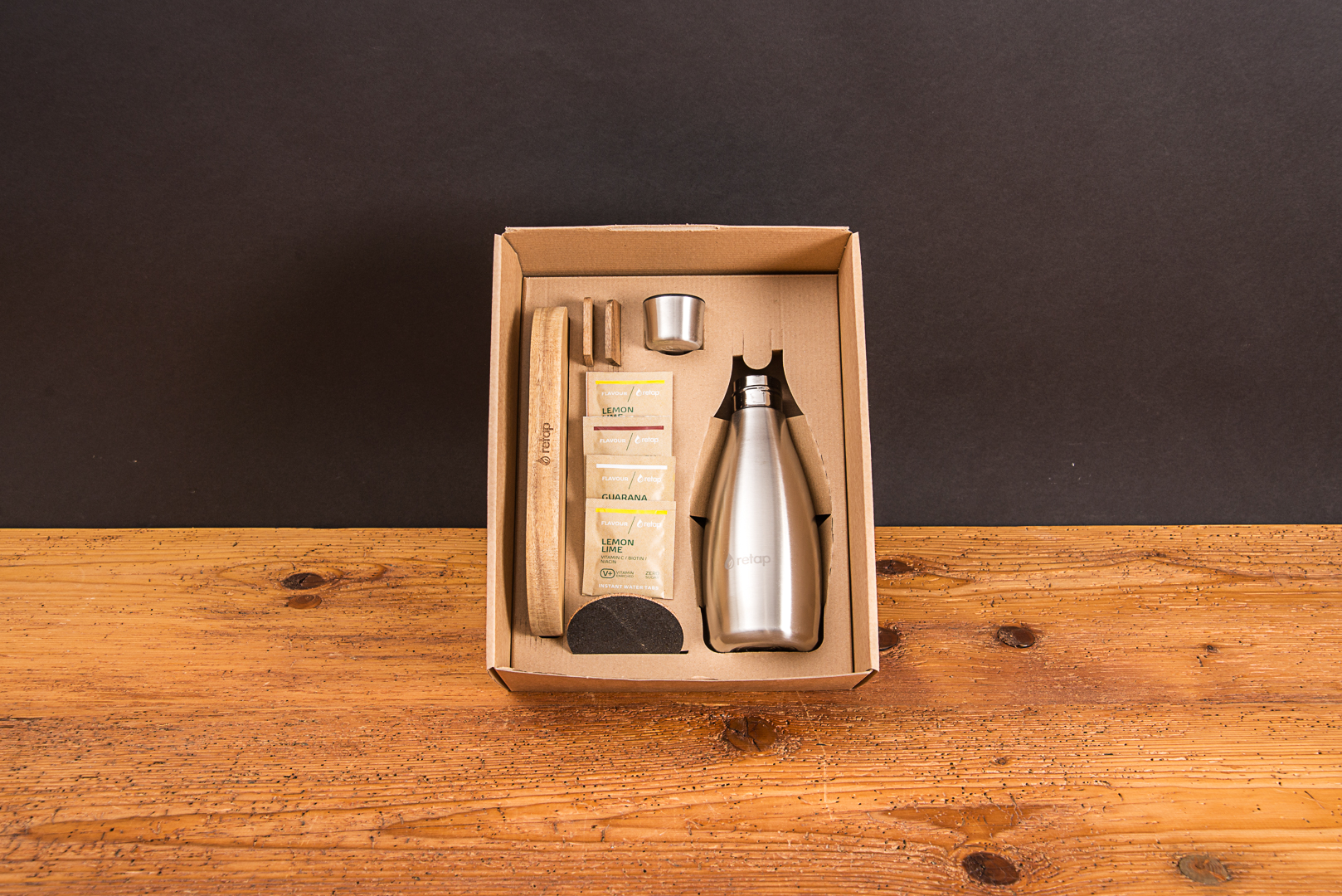 Nachhaltiges Onboarding-Geschenk Set von retap mit Eichenholz-Tray und Edelstahlflasche in einem umweltfreundlichen Karton auf einem Echtholztisch pr&auml;sentiert von werbemax.