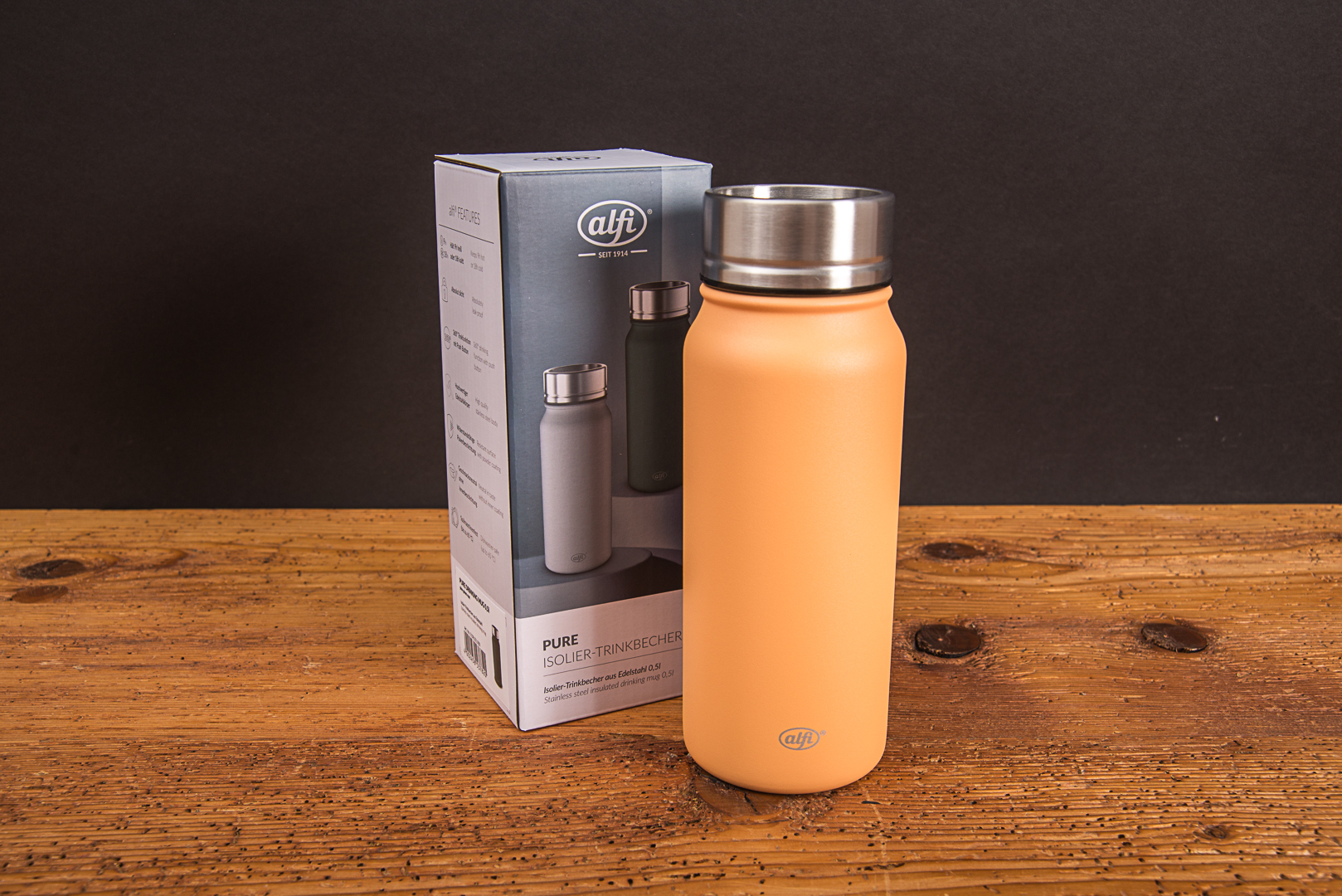 Der sunset orange alfi Pure Drinking Mug Thermosbecher stehend neben seiner originalen Karton-Geschenkverpackung auf einer Holzoberfl&auml;che als repr&auml;sentatives und hochwertiges Kundengeschenk von werbemax.