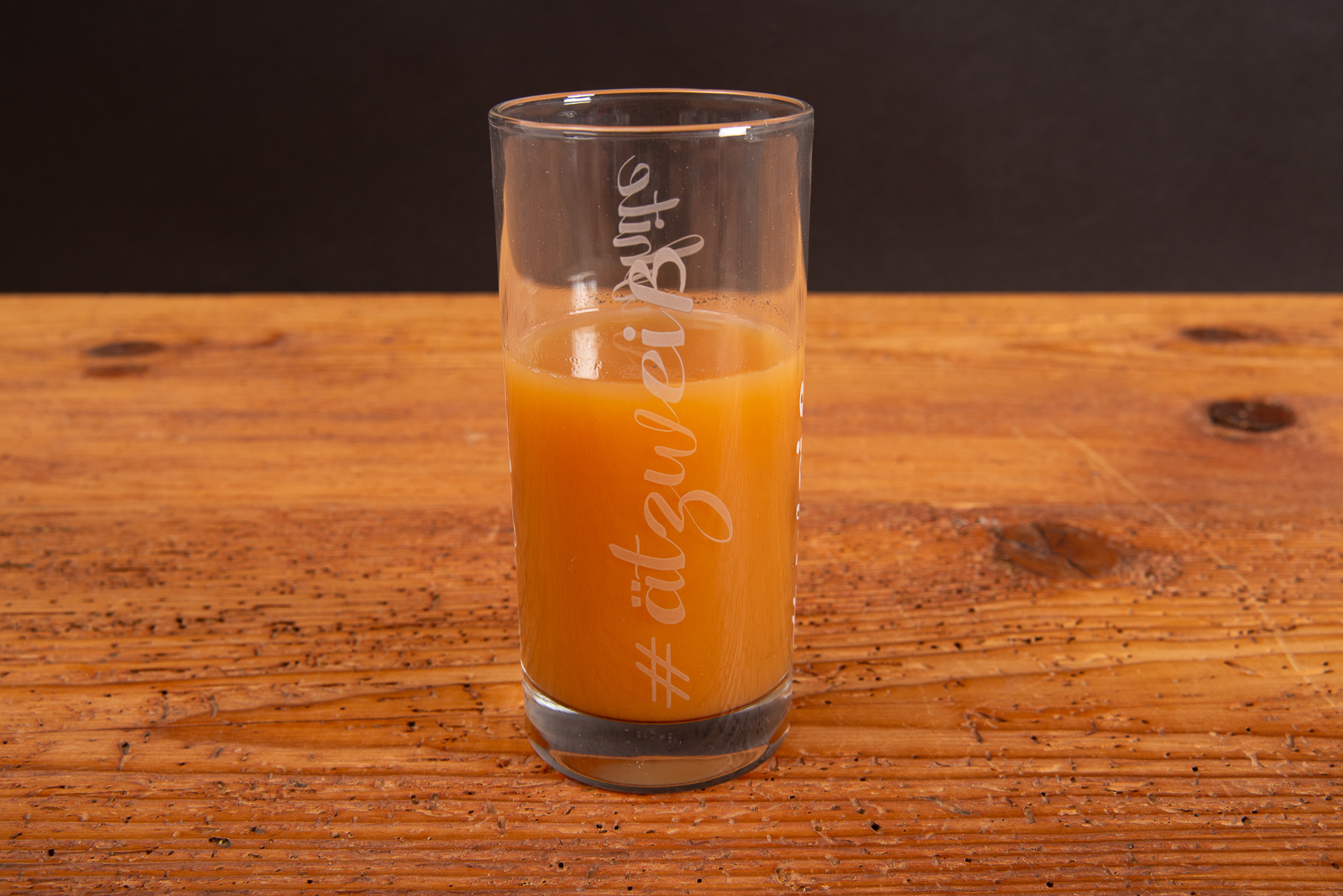 Becherglas Amsterdam 29 cl mit orangefarbenem Getr&auml;nk und wei&szlig;em Logodruck auf Holztisch