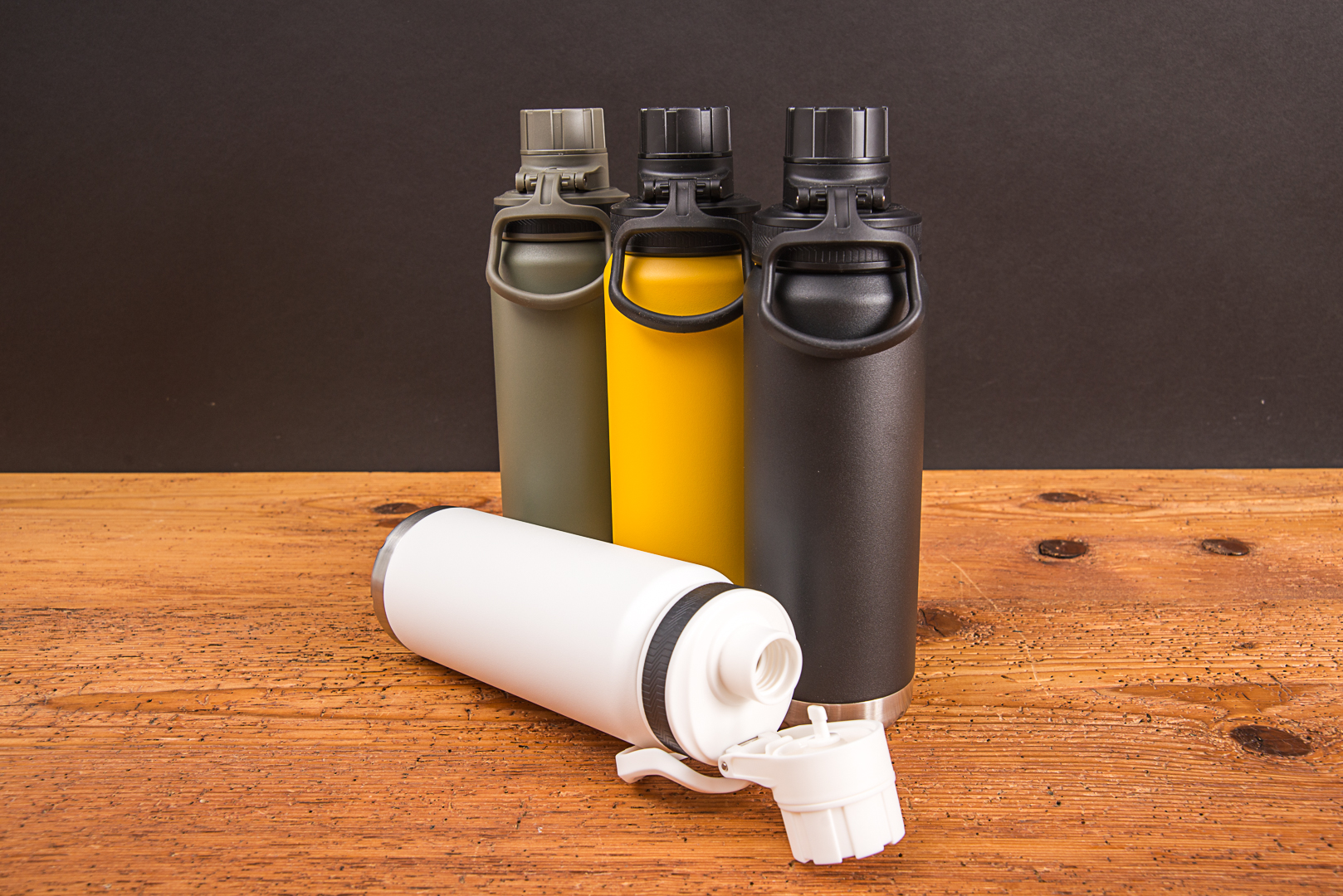 Vier Fortis 700 ml Kupfer-Vakuum-Isolierflaschen aus recyceltem Edelstahl auf Holzhintergrund in den Farben Khaki, Gelb, Schwarz und Wei&szlig; mit ge&ouml;ffnetem Schraubverschluss.