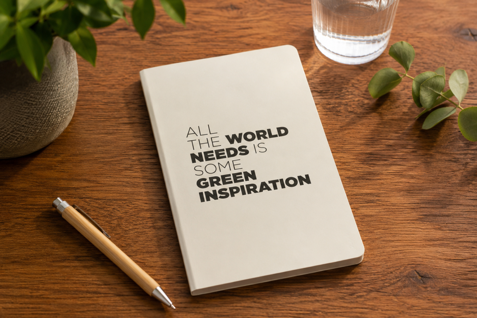Notizbuch mit inspirierendem Motiv auf einem rustikalen Holztisch, dekoriert mit Bambus-Kugelschreiber, Eukalyptuszweigen und Pflanze im nat&uuml;rlichen Workspace-Stil.