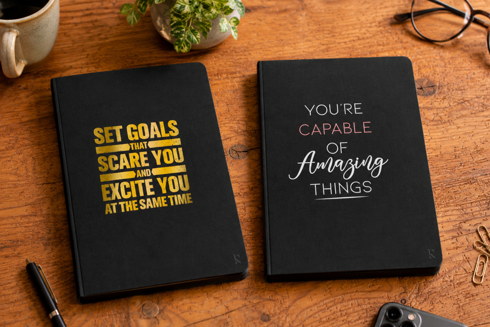 Zwei schwarze Werbemax Notizb&uuml;cher mit Motivations-Aufdruck liegen auf einem Holztisch, dekoriert mit Kaffee, Pflanze, Stift, Brille und B&uuml;roaccessoires.