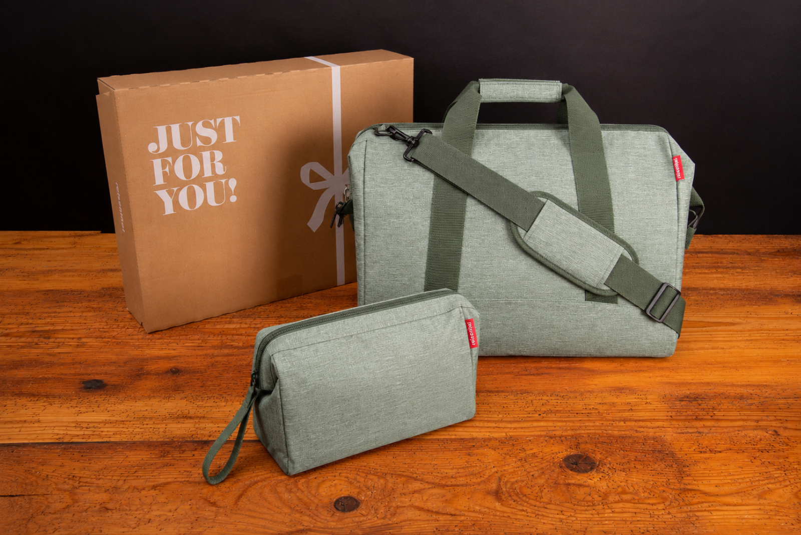 Salbeigr&uuml;ne Reisenthel Reisetasche mit Beautycase und Geschenkkarton als nachhaltiges Werbegeschenk auf Holztisch.
