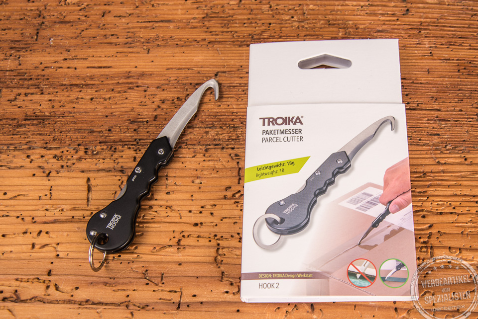 Paketmesser Troika Hook2 geöffnet liegend neben der Verpackung als Werbegeschenk.