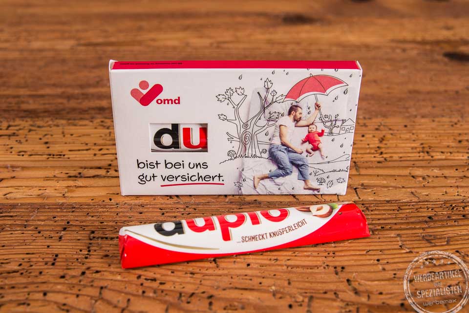Duplo Schokoriegel im individuell bedruckten Werbeschuber mit der Aufschrift &bdquo;Du bist bei uns gut versichert&ldquo; und goldenem Herzdesign &ndash; ideal als emotionales Give-away f&uuml;r Mitarbeiter und Kunden.