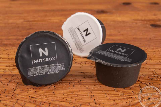Drei Snackboxen mit schwarzem und weißem Deckel mit Nutsbox Logo bedruckt. 