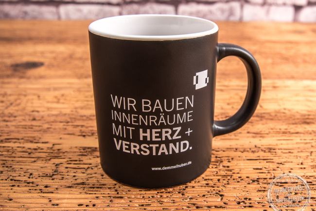 Schwarze Tasse mit weißer Werbeanbringung von Baierl + Demmelhuber