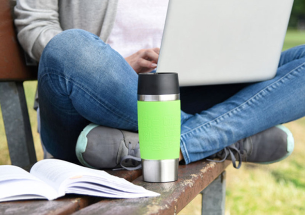 Gr&uuml;ner emsa travel mug f&uuml;r unterwegs wie hier vor einem auf einer Parkbank sitzenden am Laptop arbeitenden Mitarbeiter.