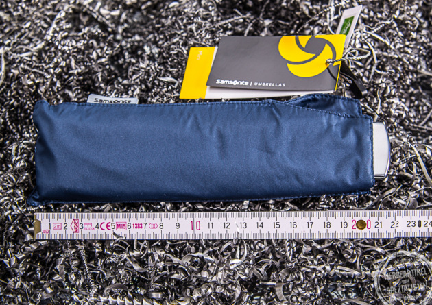 Kompakter Reiseschirm der Marke Samsonite in der Farbe Blau, in der Hülle verpackt neben einem Meterstab, um die geringe Größe noch besser darzustellen.