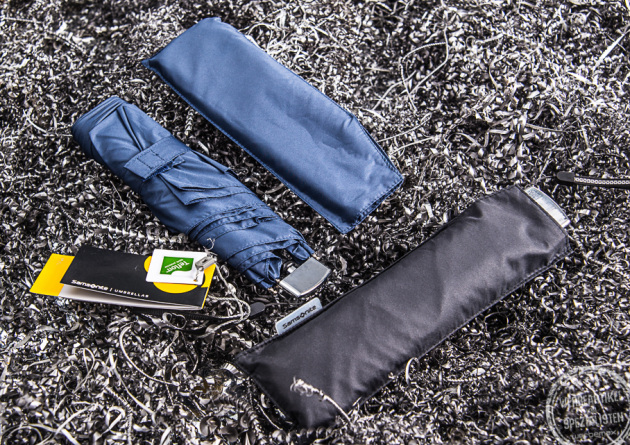 Blauer und schwarzer Samsonite Mini Taschenschirm Rain Pro liegen nebeneinander. Der blaue Taschenschirm ist aus der Hülle genommen