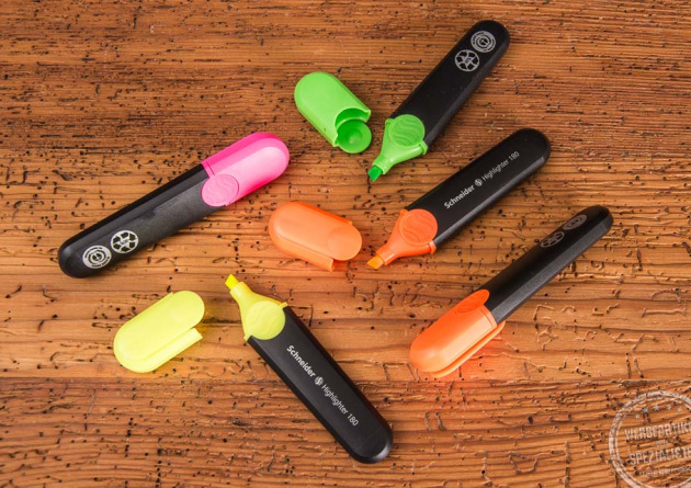 Vier Textmarker der Marke Schneider in Schwarz mit pinkfarbener, gelber, orangefarbener und gr&uuml;ner Kappe. Ge&ouml;ffnet auf einer Holzunterlage