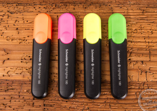 Die vier Standardfarben der Textmarker nebeneinander. Orange, Pink, Gelb und Grün liegen auf einem Holztisch nebeneinander