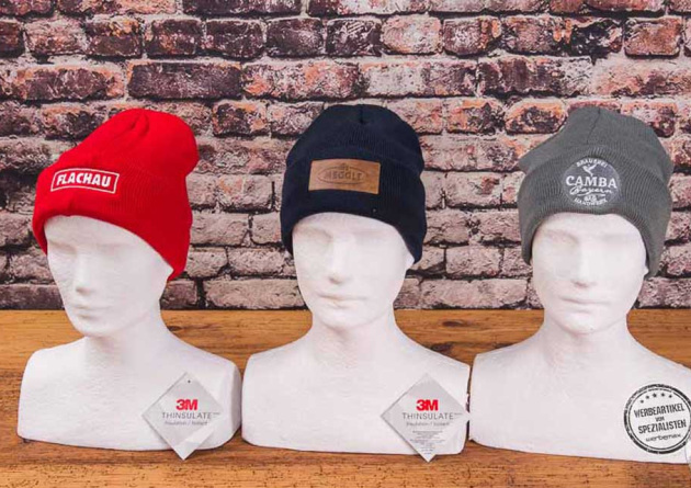 Drei Styroporköpfe mit drei unterschiedlichen Beanie Mützen in den Farben rot, schwarz und grau inkl. Logoanbringung.