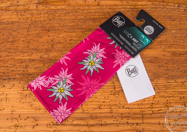 Pinkfarbenes Sportstirnband von BUFF mit Edelwei&szlig; und Karton-Hangtag als Kundengeschenk auf Holztischplatte