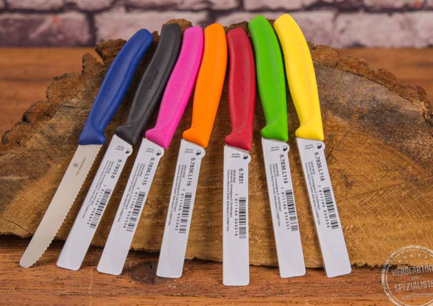 Sieben unterschiedlich bunte Tomatenmesser von Victorinox auf einer Baumscheibe liegend.