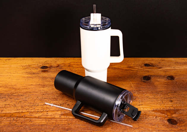 Ein stehender Tumbler creme und davor ein liegender Tumbler schwarz als Werbeartikel.