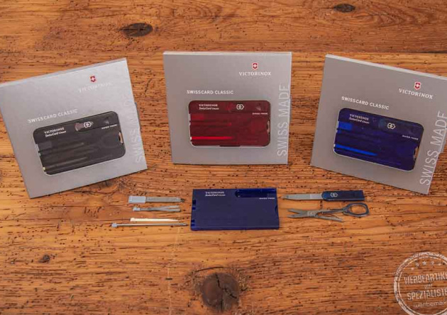 Vier unterschiedlich farbige SwissCards von Victorinox liegend auf einer Holzplatte als Werbeartikel.