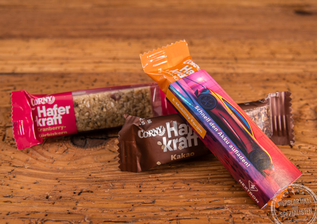 Corny Haferkraft Riegel als Give-away auf Messen im individuell bedruckten Kartonschuber auf Holztisch.