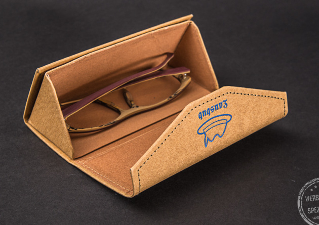 Ein Brillenetui aus Kraftpapier mit Logodruck als Werbegeschenk auf schwarzem Hintergrund.