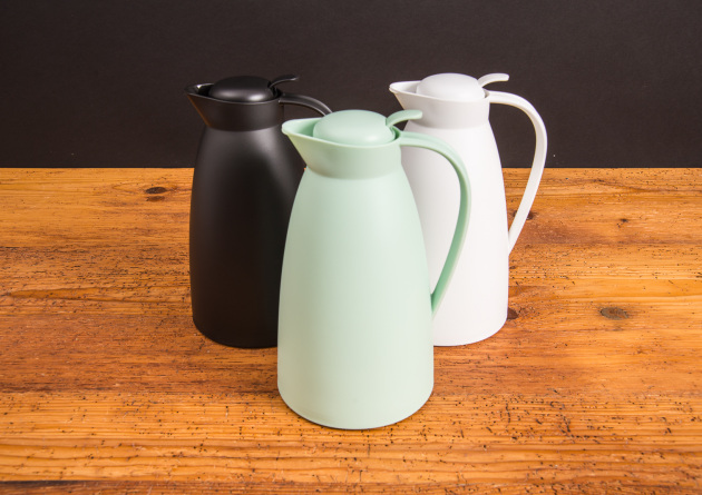 Drei alfi Isolierkannen ECO in Schwarz, Wei&szlig; und Mintgr&uuml;n auf Holztisch &ndash; stilvolle Thermoskannen als nachhaltige Werbeartikel mit Logo.